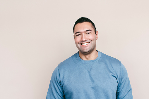 A young man standing against a wall smiling