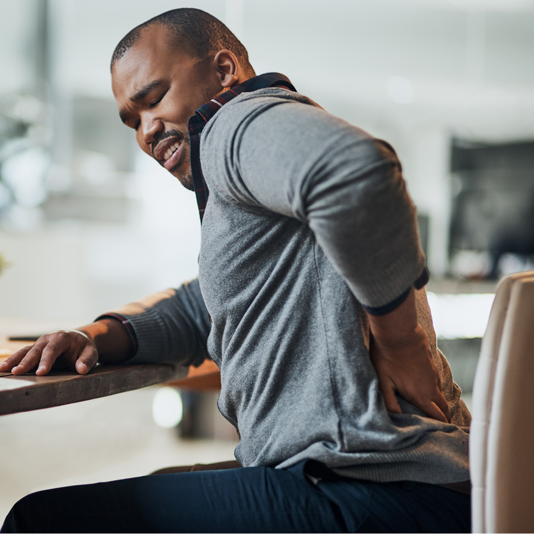 African American man at desk holding his back in pain