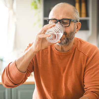 Man wearing orange drinking glass of water