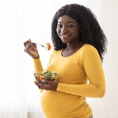 Pregnant woman wearing yellow eating a salad