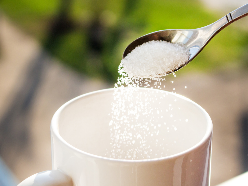 Pouring granulated sugar into a white coffee mug