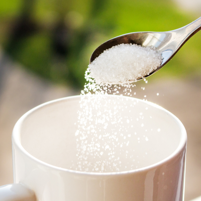Pouring granulated sugar into a white coffee mug