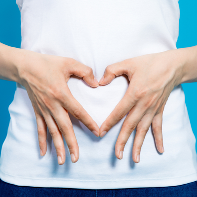 Young woman who makes a heart shape by hands on her stomach.
