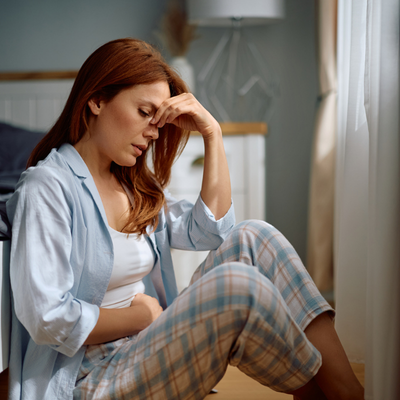 Distraught woman holding her abdomen in pain while sitting on the floor in bedroom
