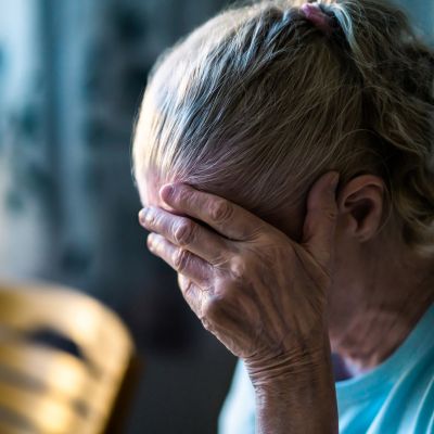 An older woman holding her head in her hands sadly