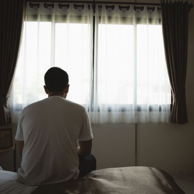 A young man sitting alone in a dark bedroom