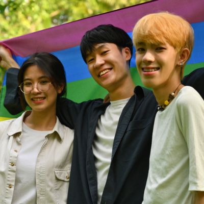 A group of people standing in front of a LGBTQ flag