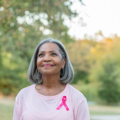 An older woman with a pink ribbon pinned to her shirt for breast cancer awareness