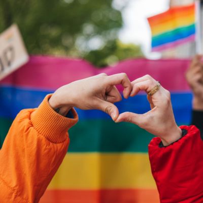 hands form a heart around LGBTQ flag