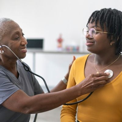A woman doctor using a stethoscope to listen to a woman's breathing.