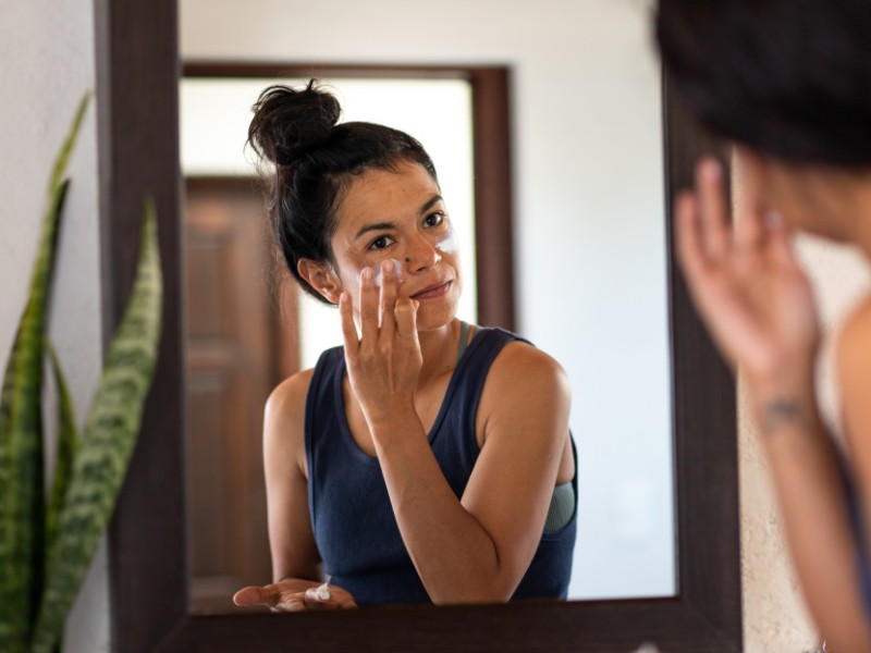 Woman putting on sunscreen in mirror