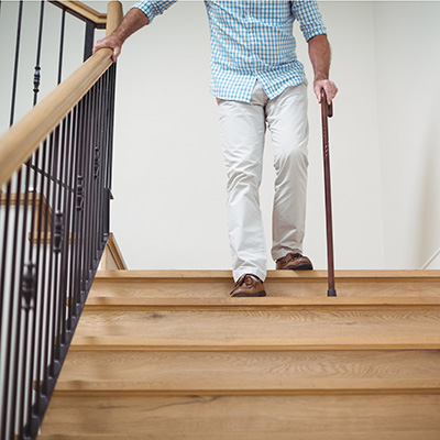 man coming down the stairs with cane and hand on rail