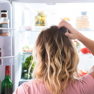 Woman staring into an open refrigerator 