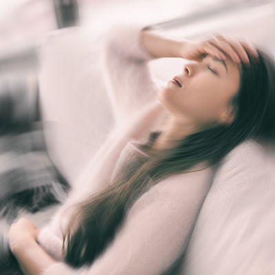 Woman on couching holding her head with blurring surroundings