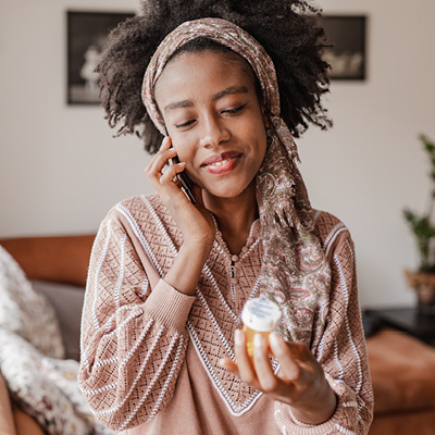 woman with a smile on the phone looking at a pill bottle