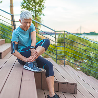 putting-best-foot-forward Older woman siting down holding her ankle in running gear