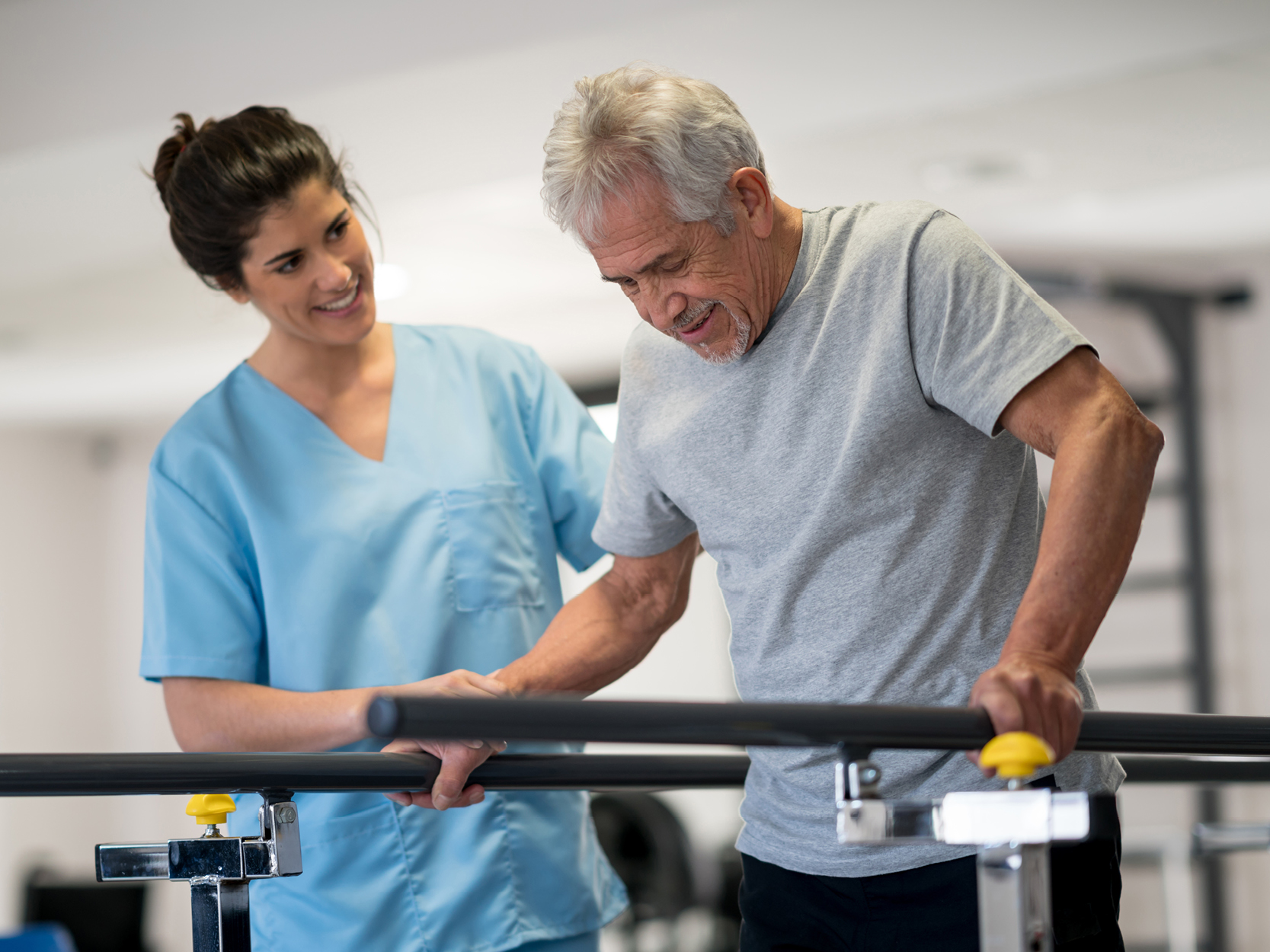 Nurse helping senior man use parallel walking bars