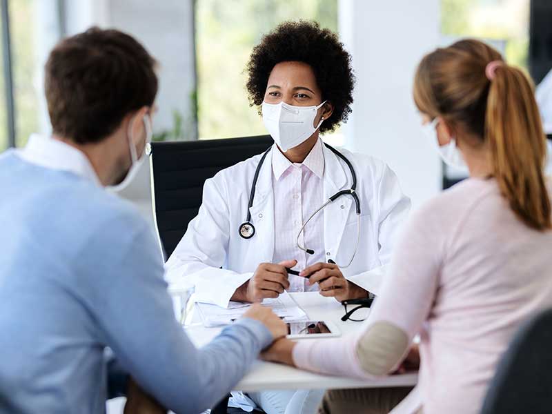 Black female doctor speaking with couple