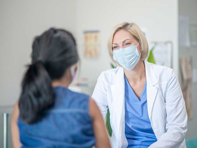 Masked Female Physician speaking with woman patient